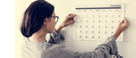 Woman wearing eye glasses hangs up a calendar on her wall